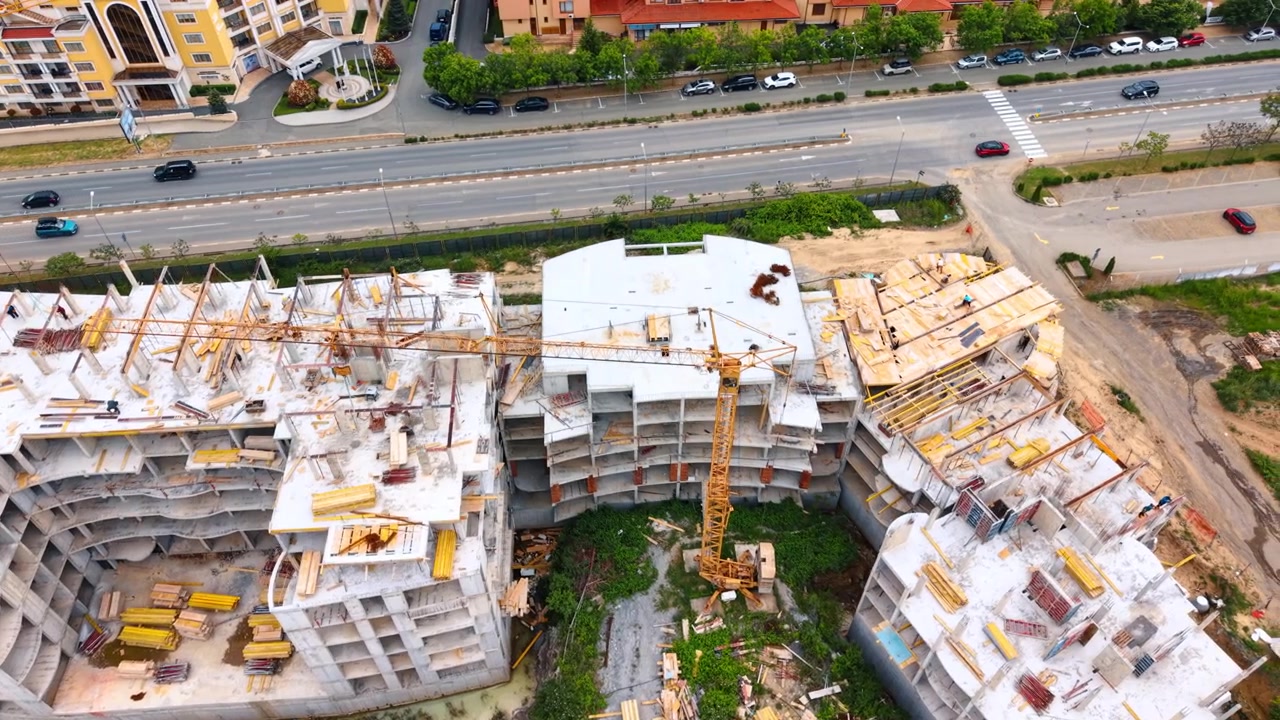 Aerial view of residential building construction site with crane. High angle drone shot of multi story concrete building framework and yellow tower crane at a construction site.