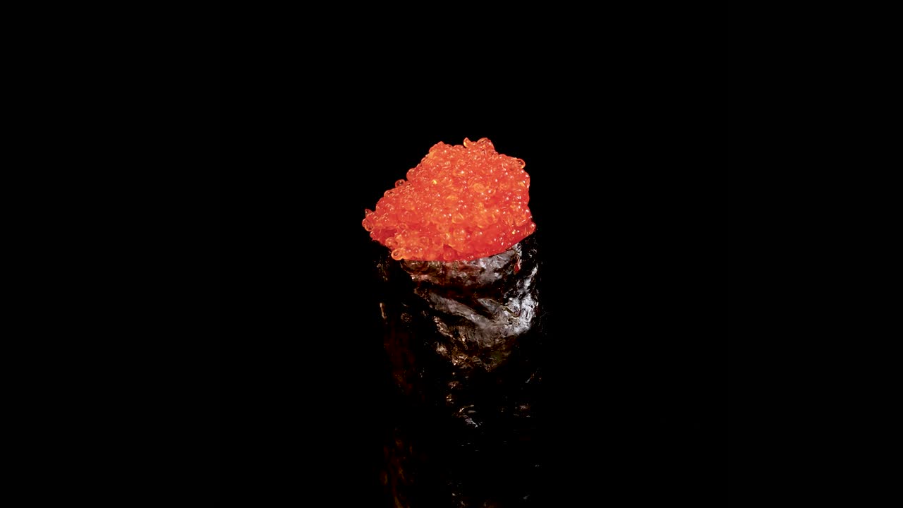 A single piece of gunkan maki sushi topped with bright orange fish roe rotates smoothly against a seamless black background, under even studio lighting