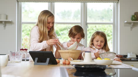 crianças de pijama fazendo panquecas na cozinha em casa seguindo a receita no tablet digital