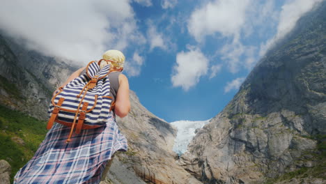 an active successful woman stands on a rock looks at the mountains and the glacier on top