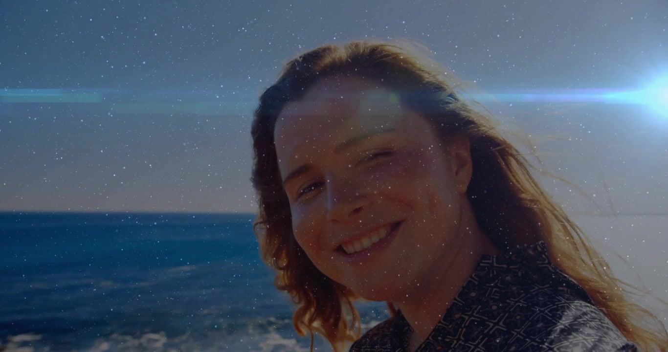 Donna che inclina la testa verso la costa rocciosa del mare, il sole causa bagliori dell'obiettivo, capelli che fluttuano, per marketing tecnologico