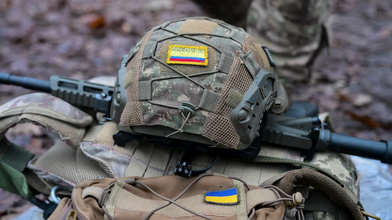The gear of a Colombian volunteer in Ukraine's International Legion, featuring Colombian and Ukrainian flags on a helmet and rifle, is shown during a tactical training exercise