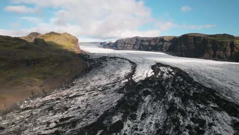 Aerial-rise-over-Iceland-glacier-sweeping-through-mountain-valley,-sunny-day