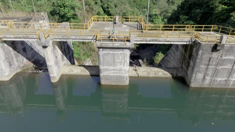 Toma-Aérea-Inclinada-Hacia-Abajo-Del-Edificio-De-Construcción-De-La-Presa-Tireo-Con-Agua-Verde-En-Bonao