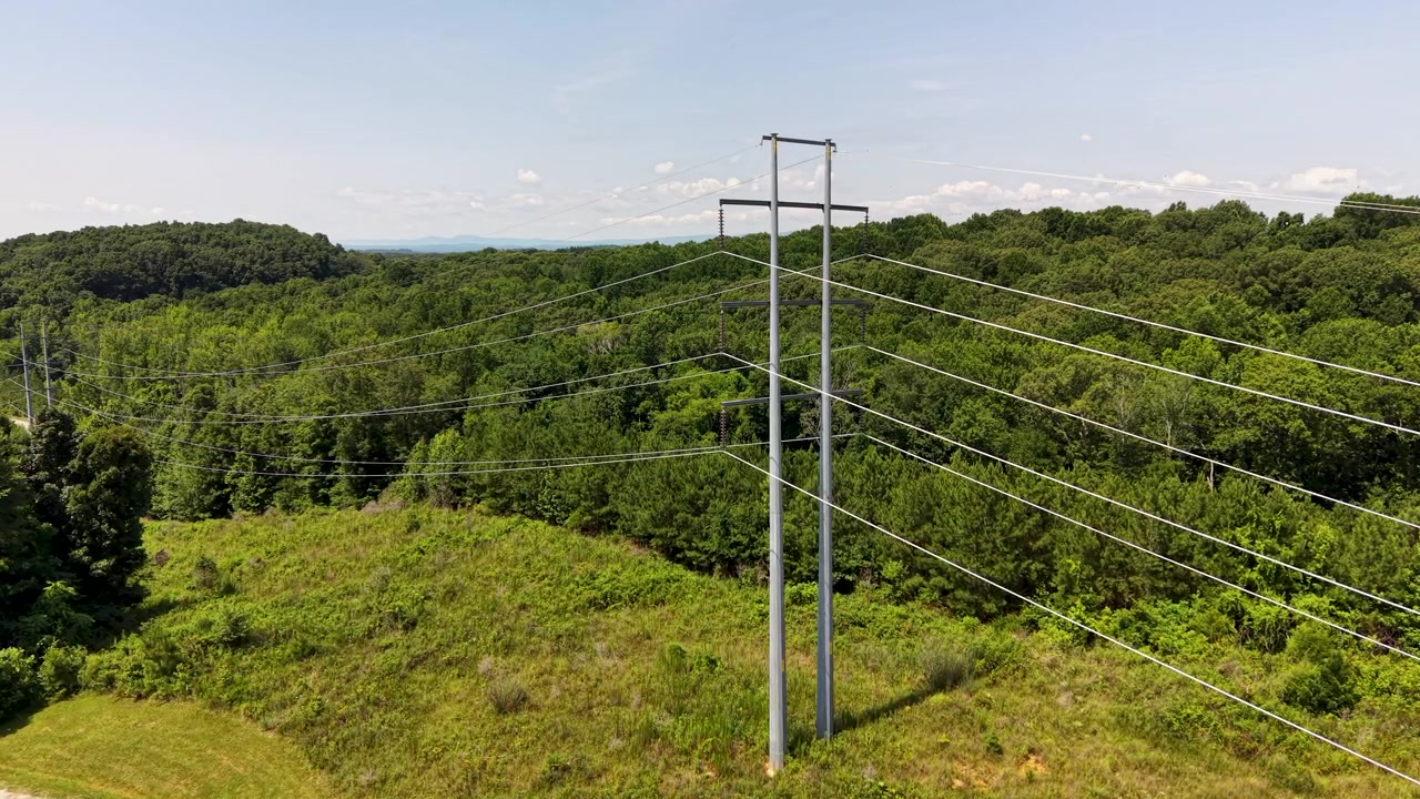 High-voltage transmission corridor near Chattanooga, Tennessee, United States, revealing steel monopoles, polymer insulators, overhead conductors and deciduous woodland, drone push-in.