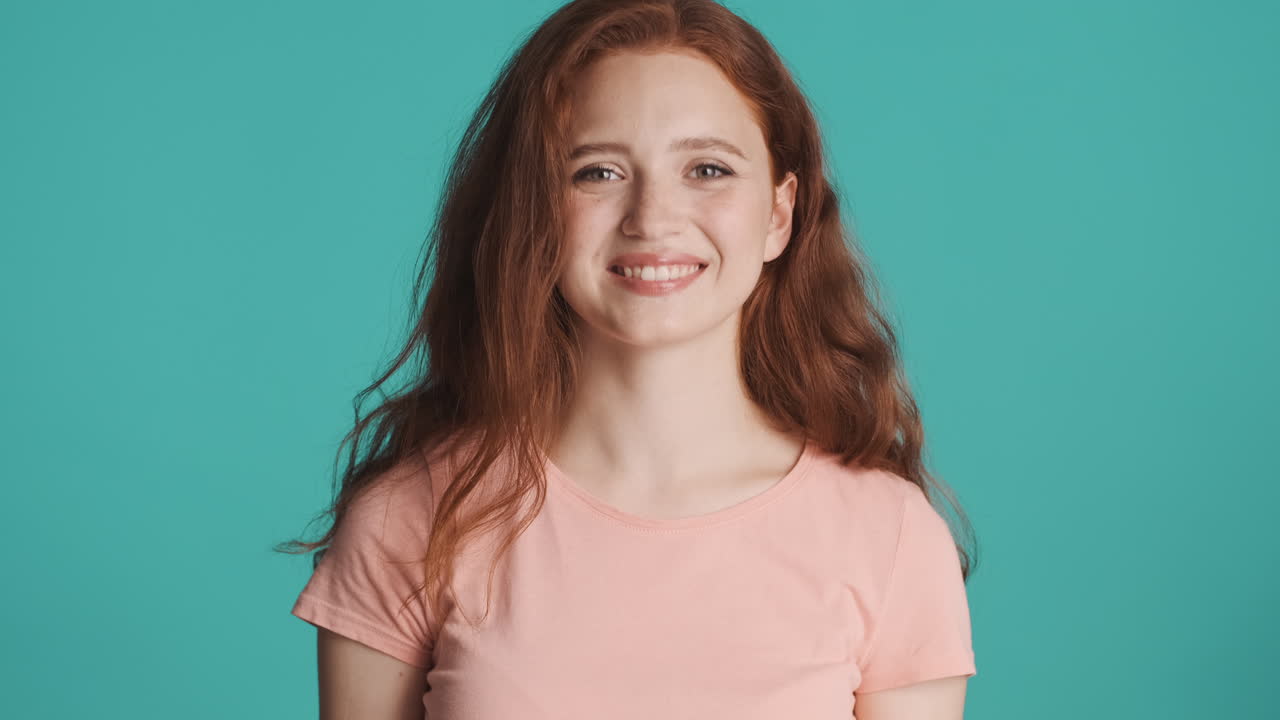 은 머리의 소녀가 르키즈색 배경에서 카메라를 보고 있습니다.