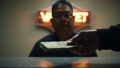 an intense scene at the front desk of a motel: the interaction between a customer and the attendant with cash on the table and a 'vacant' sign in the background