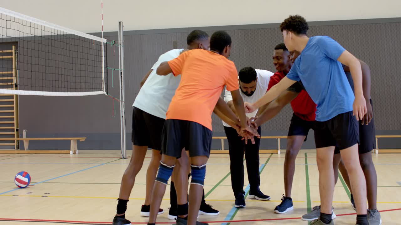 Reacting to captain signal Diverse male teammates huddling beside net on court preparing to play