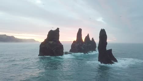 reynisdrangar rocks at reynisfjara beach next to vik i myrdal at south iceland. aerial drone shot flying over a cliff during sunrise. large storm waves crash rock. high resolution footage. 4k
