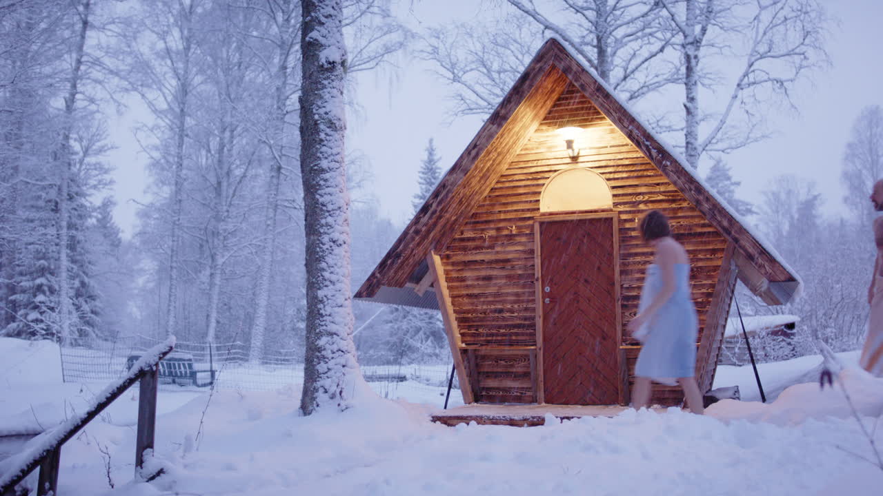 Scandinavian couple in towels enter cute wooden sauna in fairytale snowy woods
