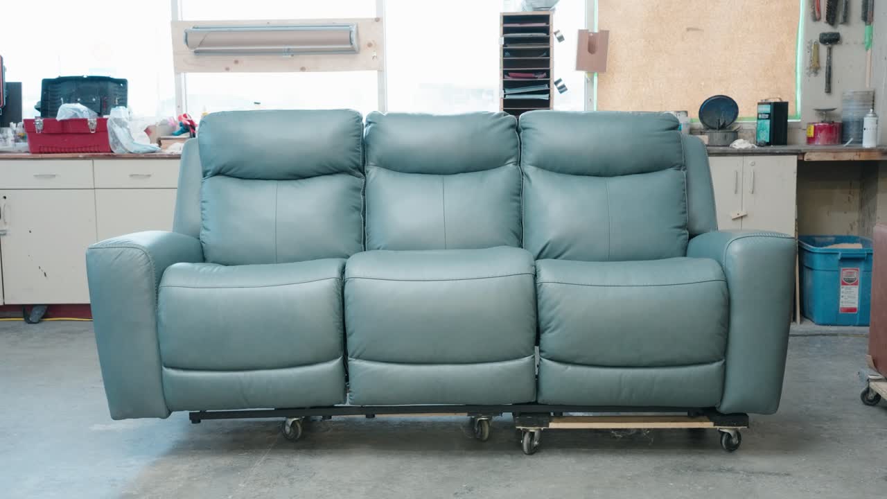 Camera glides toward blue leather sofa on rollers amid workshop shelves
