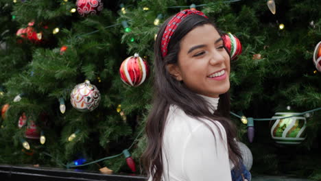 mujer joven de compras navideñas en la ciudad con un árbol decorado con adornos y luces navideñas festivas