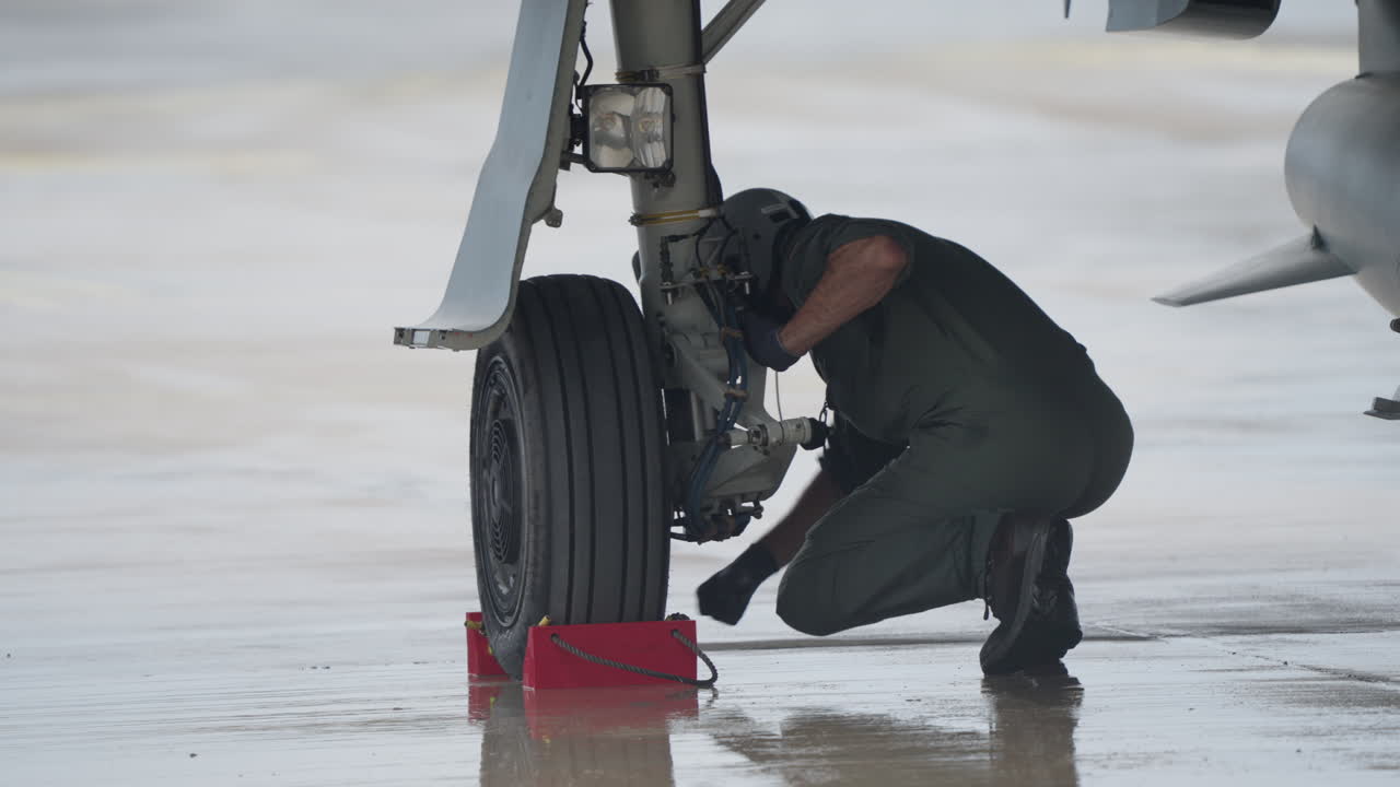 Aircraft Mechanic Inspecting Landing Gear on Wet Tarmac