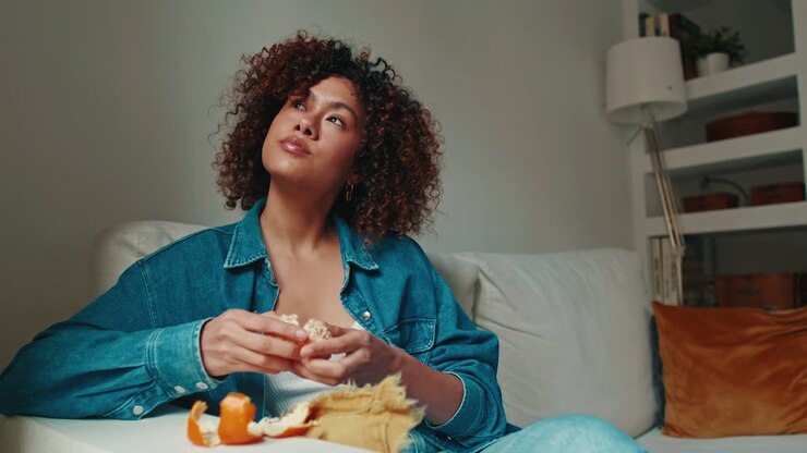 Woman eating a tangerine on a sofa