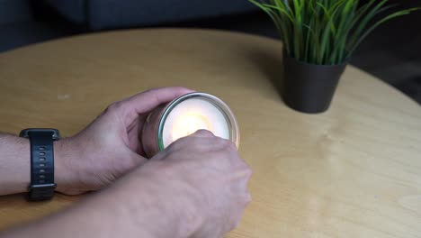 4k close-up of hands handling a white candle in a glass jar on a wooden table beside a plant. ideal for relaxation, spa, or lifestyle themes.