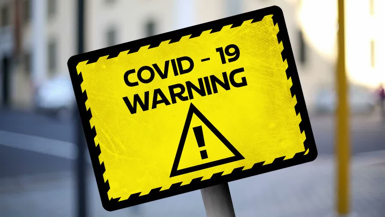 Animation of the words Covid-19 warning written on yellow sign over city street in the background.