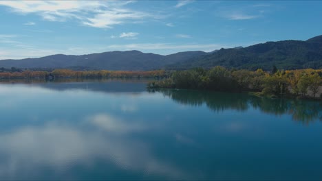 lake banyoles reflects sky and trees around it in autumn