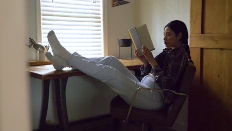 focused puerto rican female reading captivating story with feet raised resting on desk