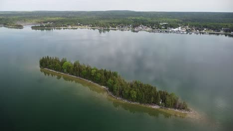 Calm-Water-Aerial-of-Lonely-Island-off-of-coastline,-Hessel,-Michigan