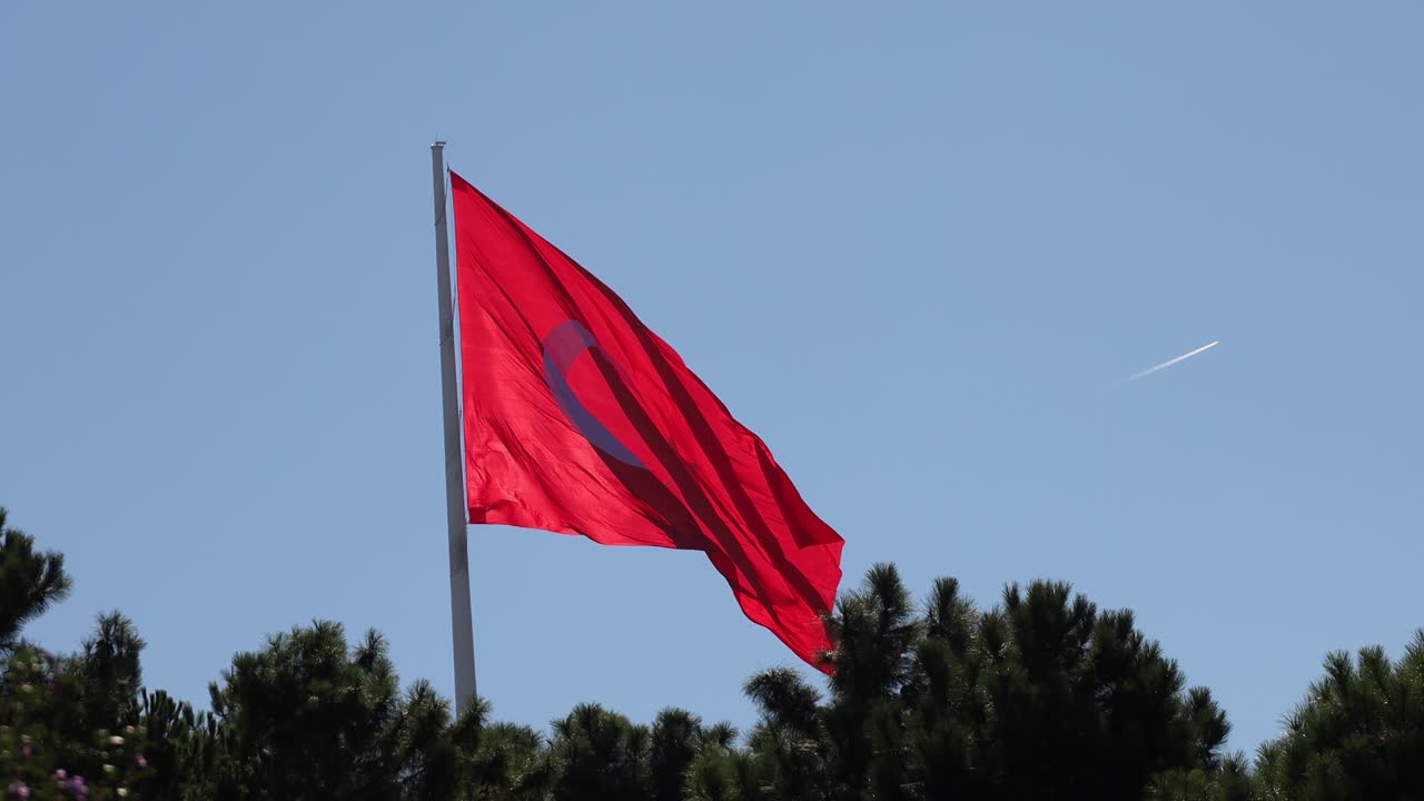 Turkiye or Turkish red flag waving in the wind on a pole against blue sky in outdoor setting