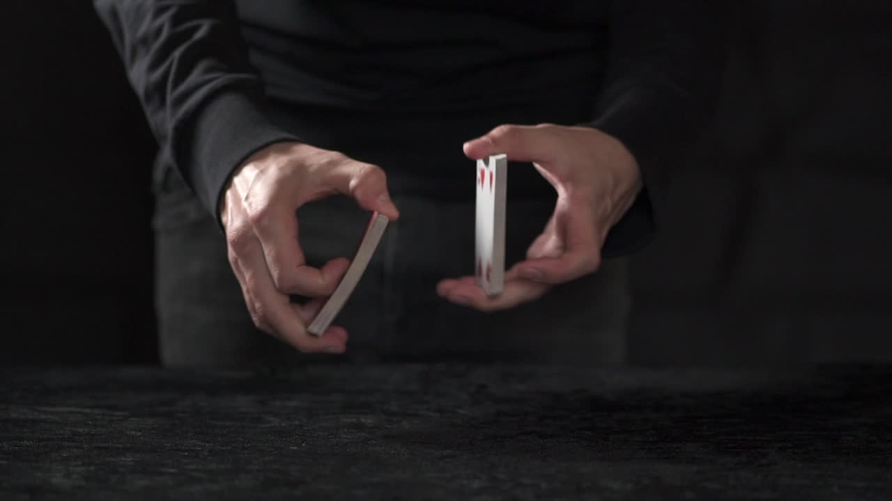MCU CÁMARA LENTA: Crupier masculino divide una baraja de cartas por la mitad y realiza un barajado americano en una mesa negra.