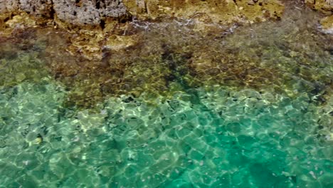 Textura-De-Agua-De-Mar-Esmeralda-En-La-Costa-Con-Rocas-Bañadas-Por-Agua-De-Mar-Tranquila-Que-Refleja-La-Luz-Del-Sol