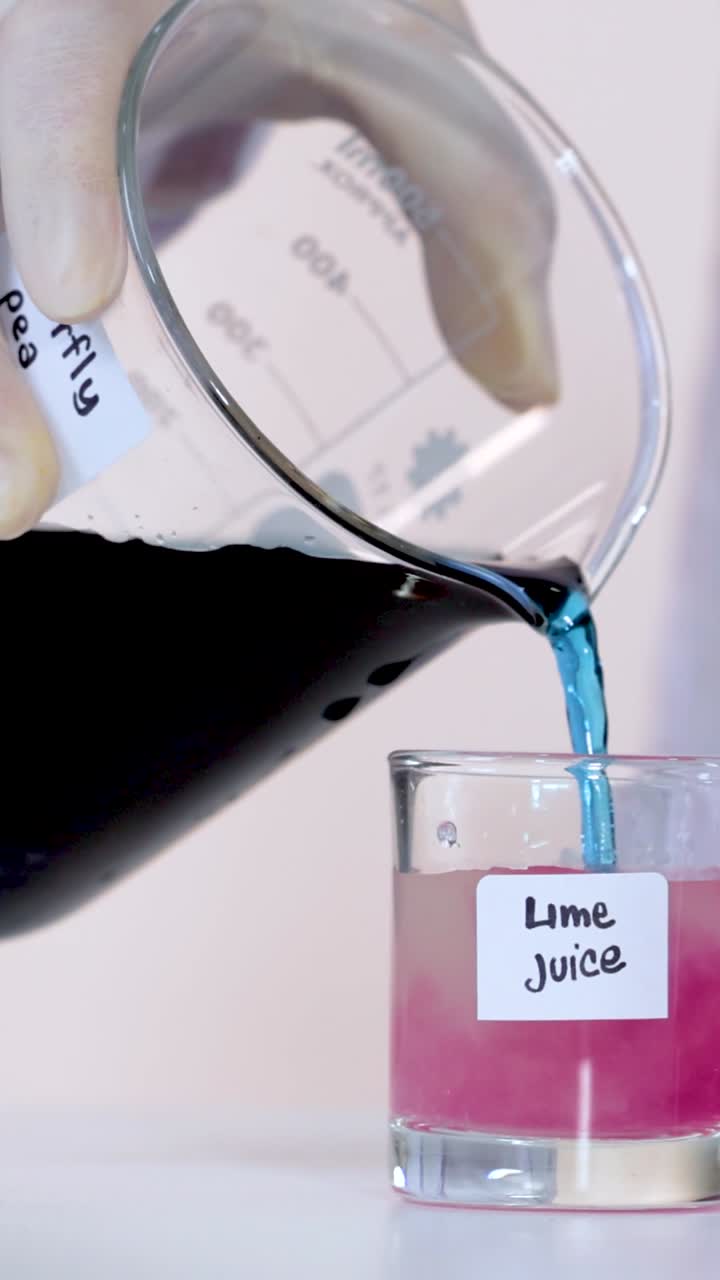 Primo piano verticale che mostra il tè blu ai fiori di pisello farfalla che diventa rosa quando versato nel succo di lime.