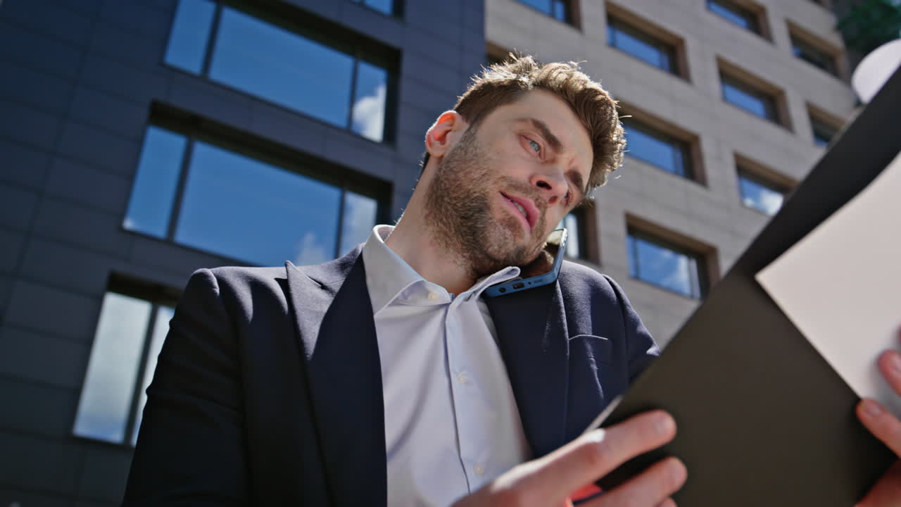 Busy employee calling mobile phone reviewing papers data on street closeup