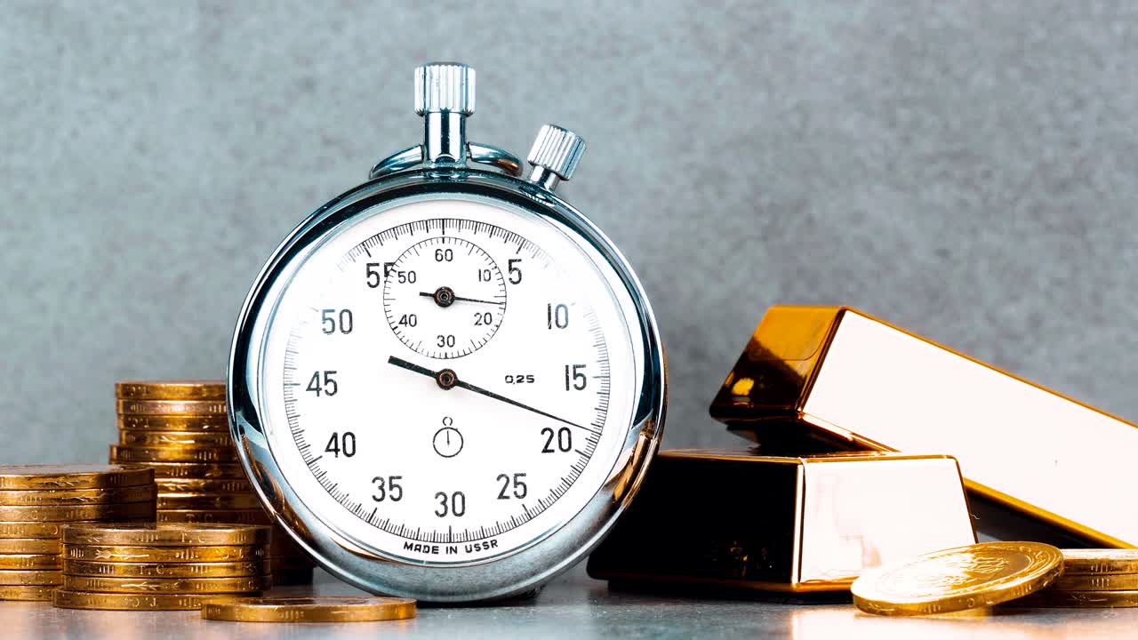 cronómetro cronómetro con monedas y bloques de oro en fondo gris