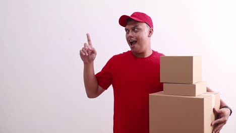 Wow-amazed-young-asian-courier-man-holding-cardboards-while-pointing-sideways