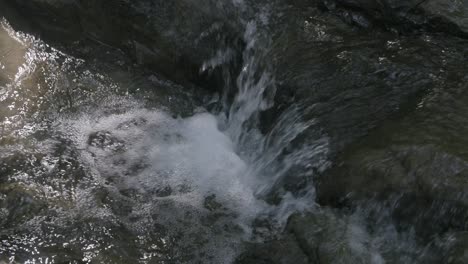Nahaufnahme-Von-Zeitlupenaufnahmen-Eines-Kleinen-Wasserfalls,-Der-Von-Einem-Felsen-In-Einem-Bach-Kommt