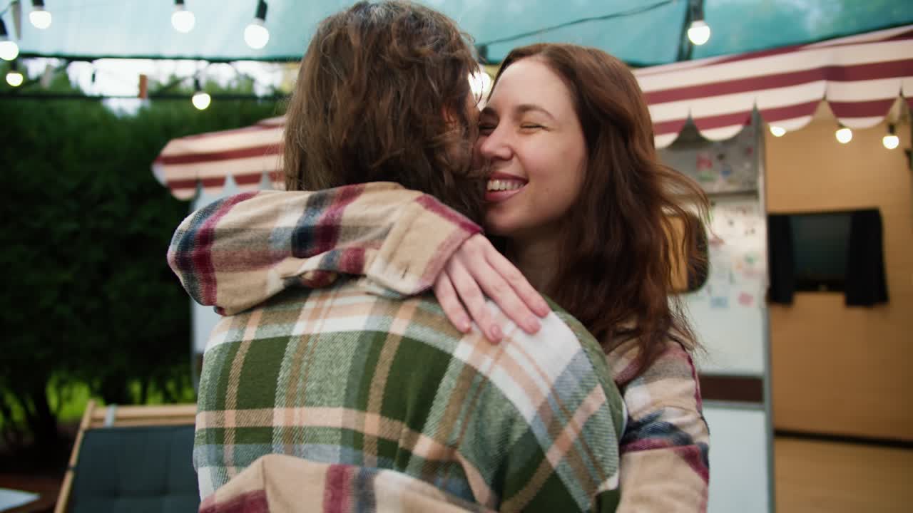 feliz chica morena con una camisa a cuadros rosa sale de su remolque y abraza a su novio moreno con una camiseta a cuadros verde durante sus vacaciones fuera de la ciudad en un campamento durante un picnic en el verano