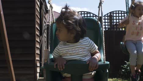 cute baby and older sister on swing together in the garden