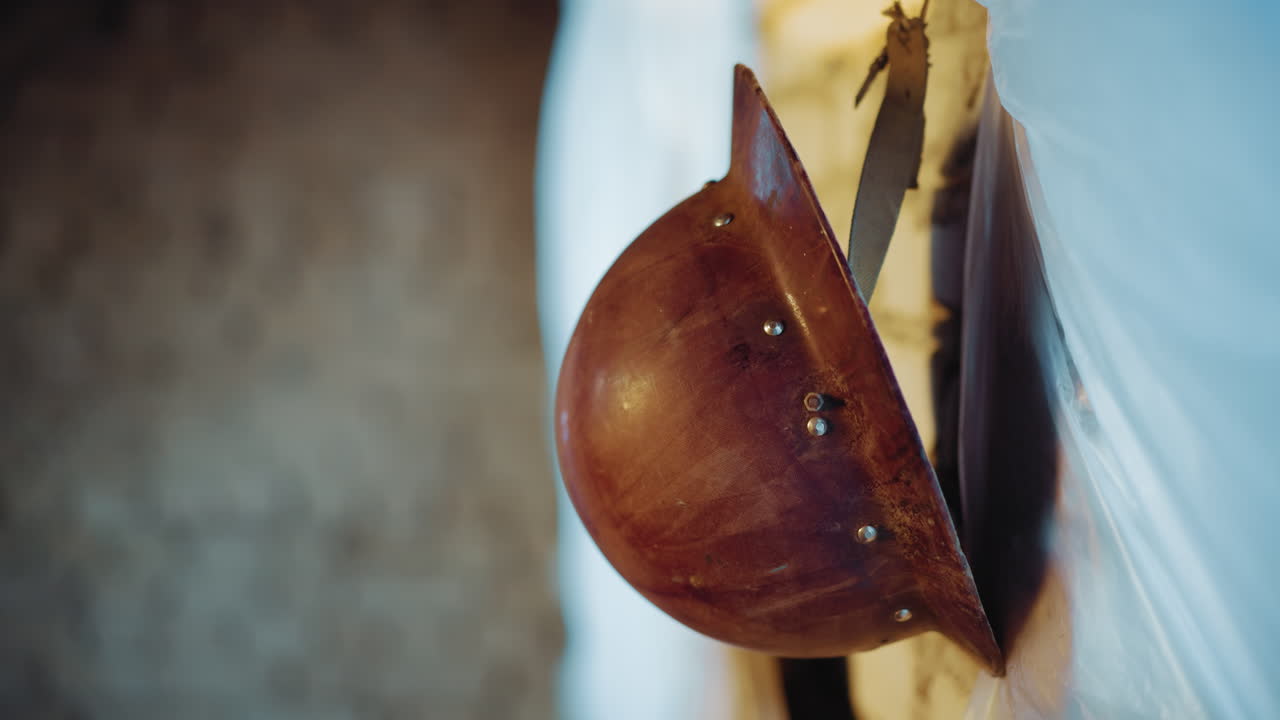 Close up of rusty military helmet hanging on strap against wall, showing aged surface, dents, and rivets, symbolizing war, protection, survival, and forgotten history with dramatic light
