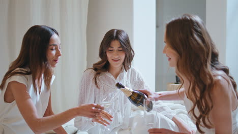 women friends pouring champagne on home party closeup. excited girls celebrating