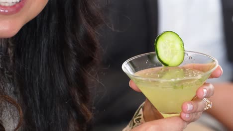 cucumber martini is held by smiling woman, closeup of hands with ring and no faces