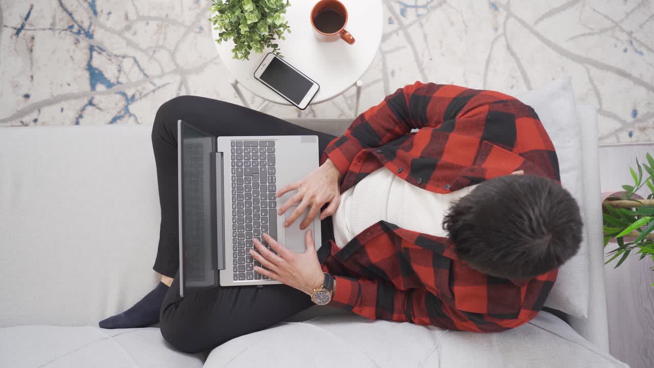 젊은 남자가 집에서 소파에서 휴식을 취하면서 노트북을 검색하고 있습니다.