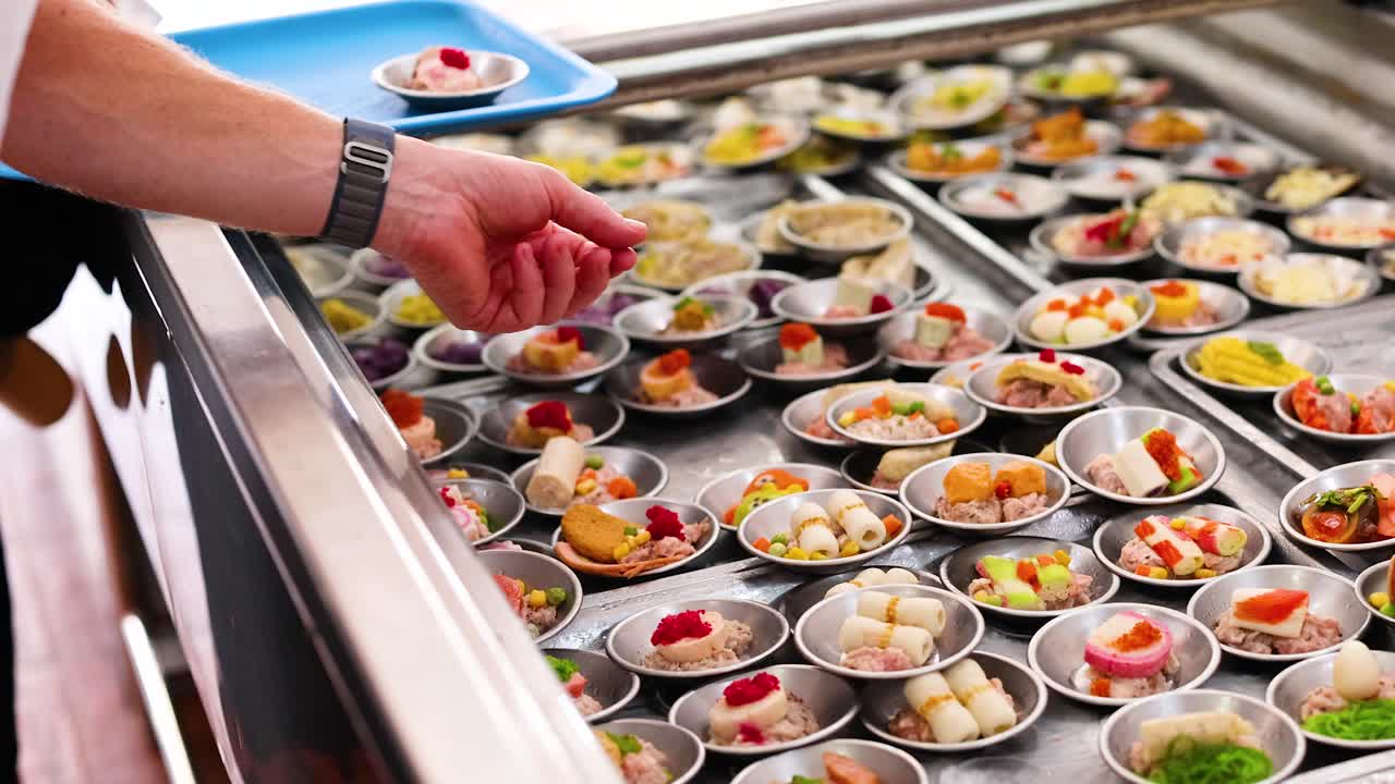 A person selects dim sum from a vibrant array at a Phuket market. Bright lighting enhances the colorful presentation