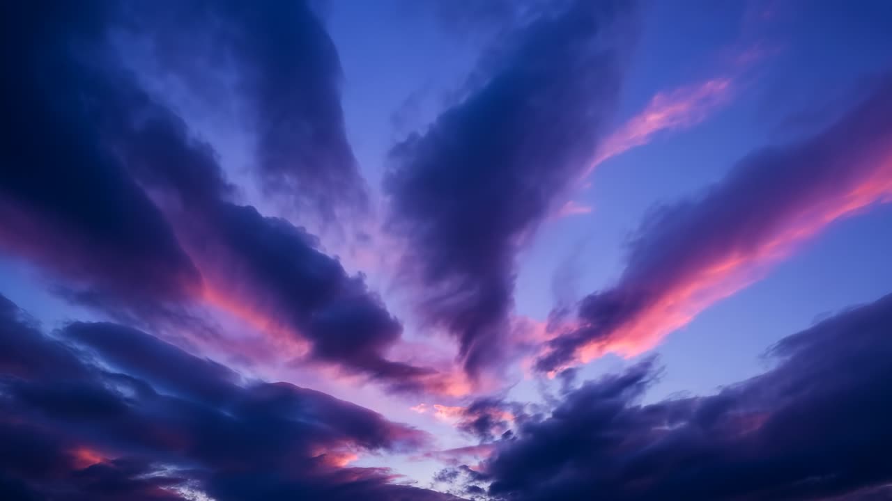 Spreading sunset glow illuminating cloud plumes at dusk over open sky, with magenta highlights