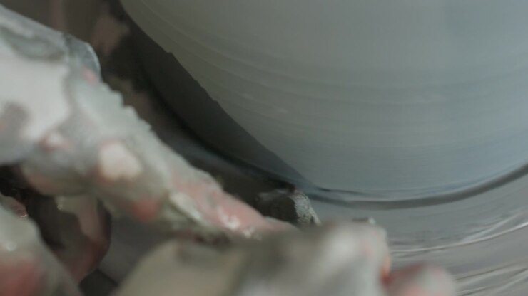 Pottery finishing touch on spinning wheel closeup, caucasian hands applying water and gentle pressure to refine rim, subtle texture and sheen, final smoothing stages, quiet tactile studio moment