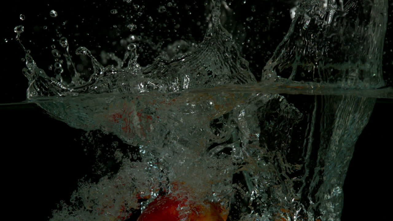 Apple orange and banana plunging into water on black background