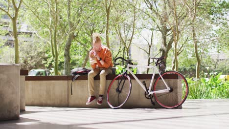 albino african american man with dreadlocks sitting in park with bike eating sandwich