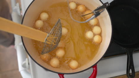 stirring donut holes frying in hot oil with spider strainer, slowmo overhead