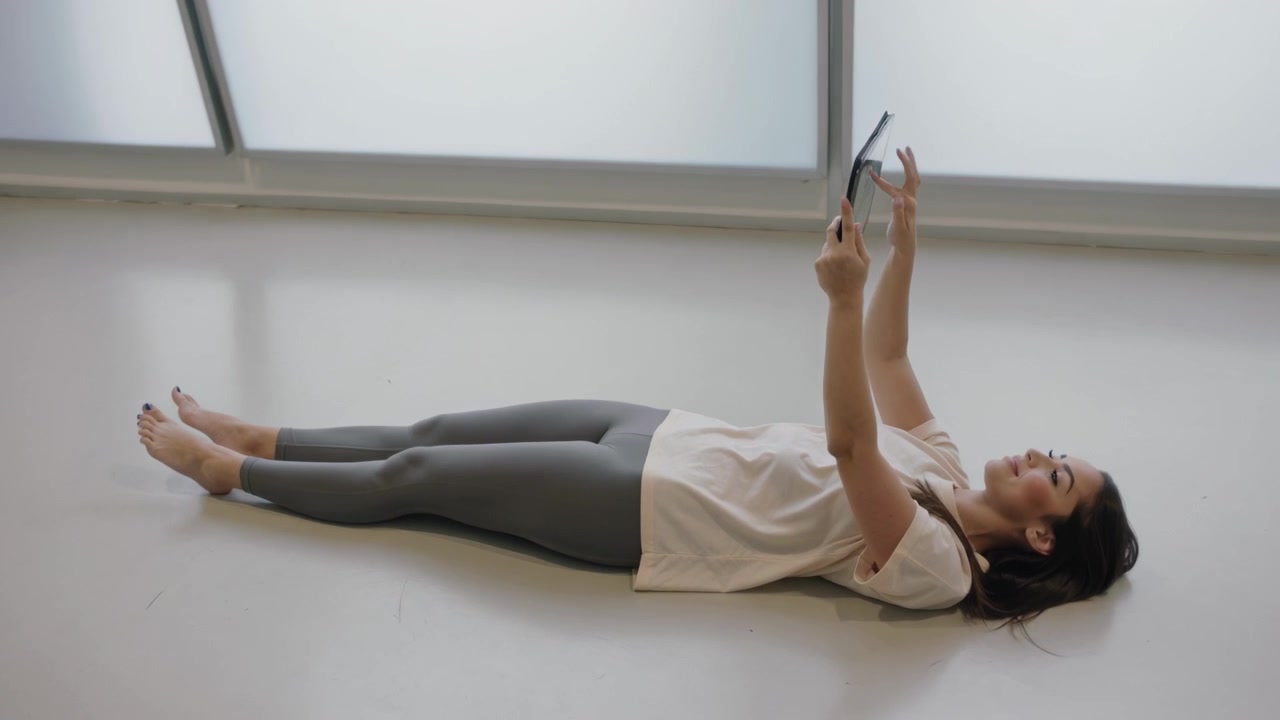 Starting tablet, woman in tee leggings adjusting, tapping screen to see content on floor by windows