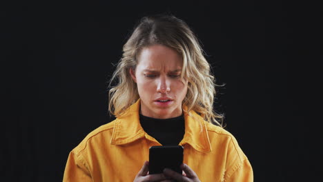 fotografía de estudio de una mujer infeliz con un teléfono móvil siendo intimidada en línea en cámara lenta