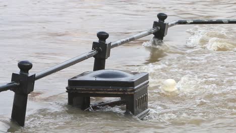 The-River-Severn-overflowing-its-banks-at-Bewdley,-covering-a-litter-bin-and-railings