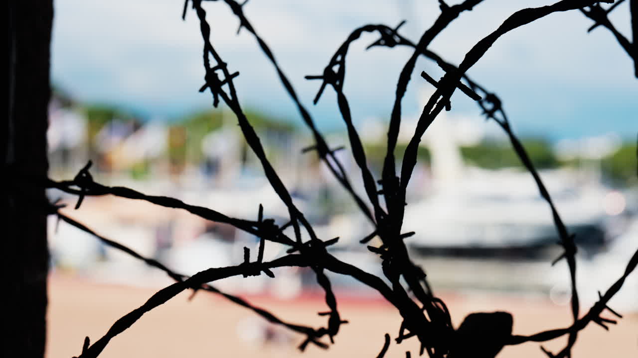 Close up of barbed wire loops with a blurred view of boats docked in a harbour in daylight