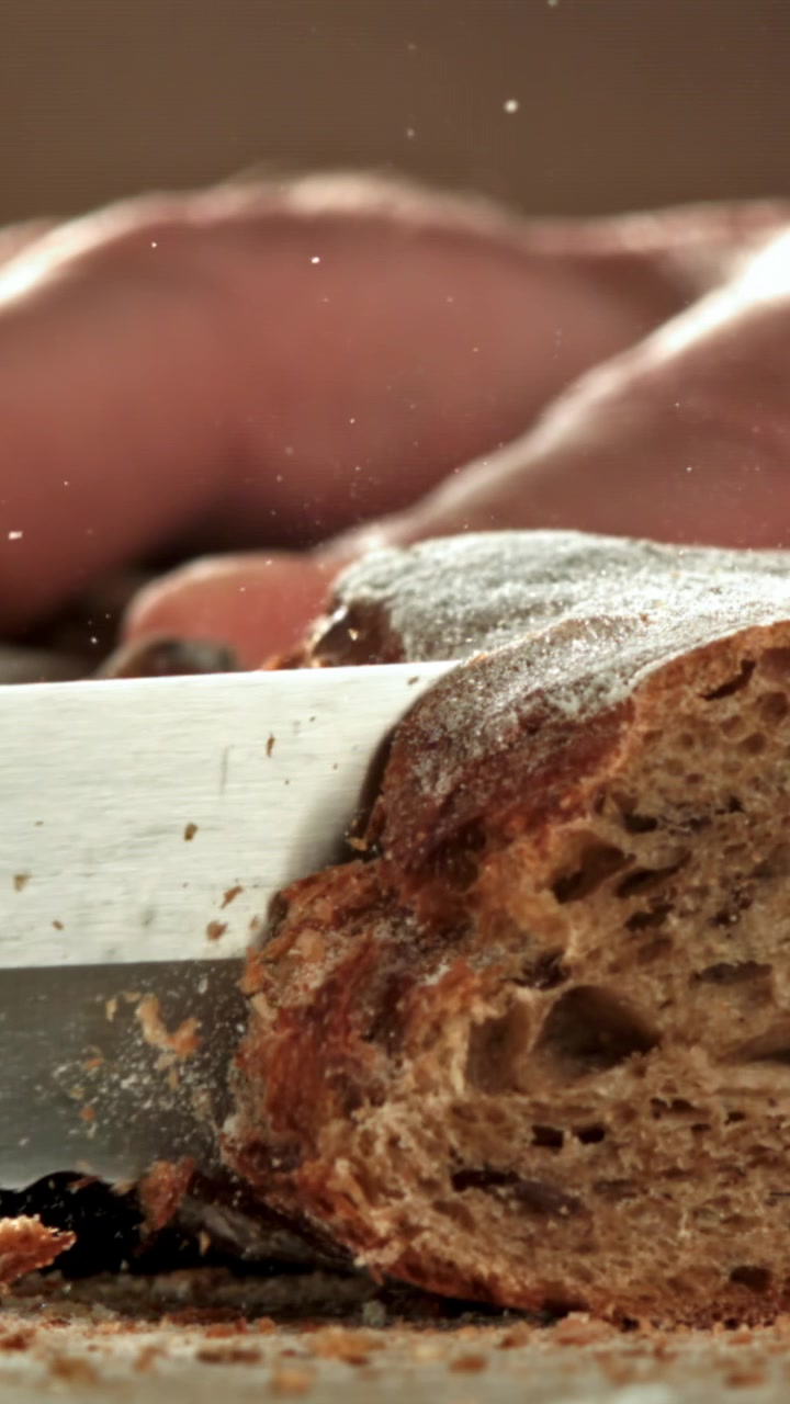 Close-up of a Knife Slicing Fresh Rustic Bread in Slow Motion