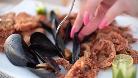 mujer caucásica sacando un mejillón de un plato de marisco.