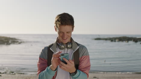 portrait-of-young-man-texting-browsing-using-phone-standing-on-beach-smiling-happy